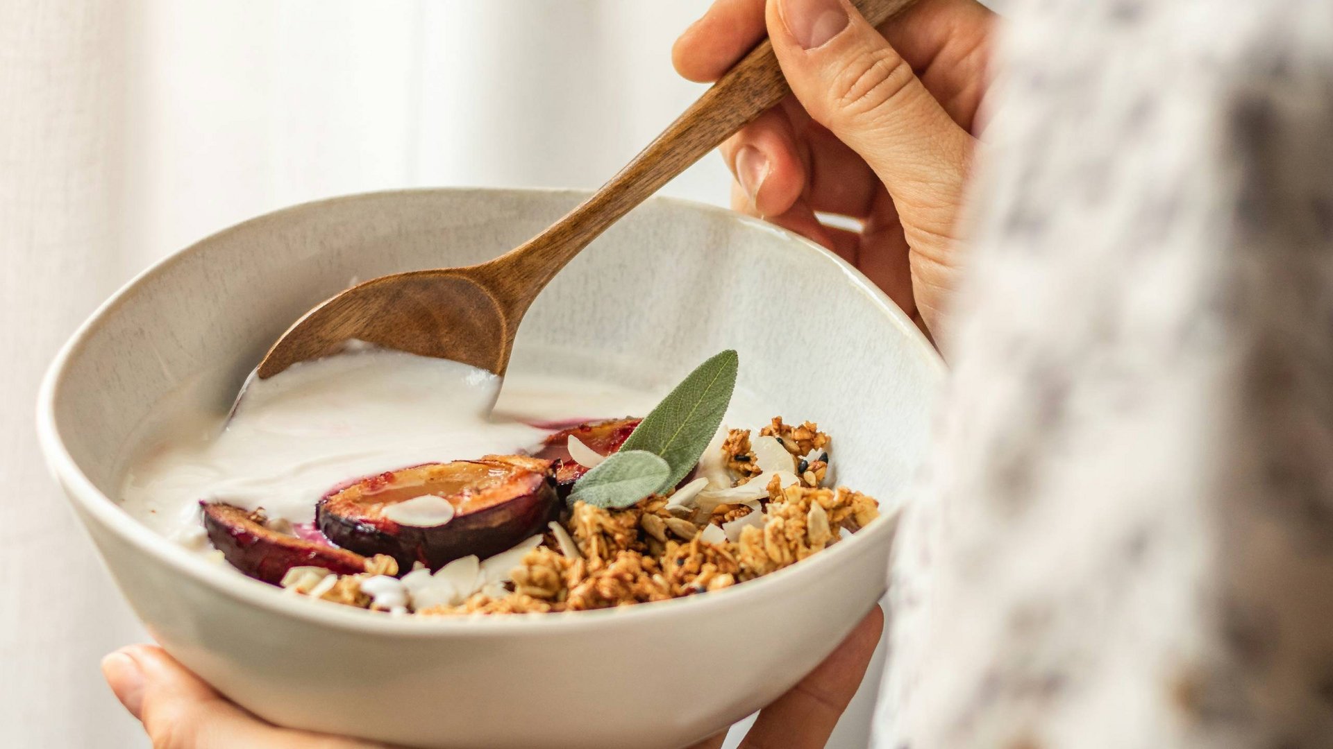 Person hält Schüssel mit Joghurt, Granola und Pflaumen