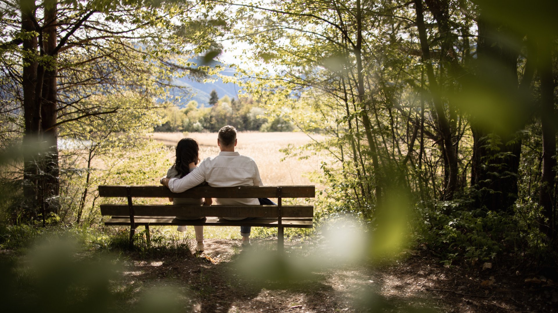 Ein Paar sitzt auf einer Bank im Wald und blickt auf das Feld
